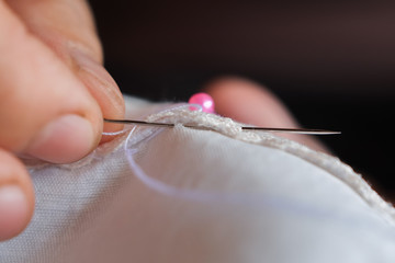 Fingers hands of the seamstress is using a needle and white thread to sew the seam on the shirt close-up.