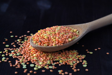 red lentils in a wooden spoon. wooden spoon with dried red and yellow lentils on a wooden table. Healthy lifestyle. close-up red and yellow lentils in a wooden spoon on a black background. copy space.