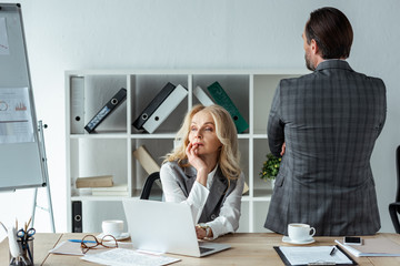 Thoughtful businesswoman looking away near laptop and businessman in office