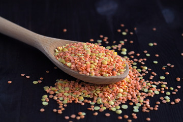 wooden spoon with dried red and yellow lentils on a wooden table. Healthy lifestyle. close-up red and yellow lentils in a wooden spoon on a black background. copy space.