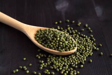  close-up mung beans in a wooden spoon. green mung beans in spoon on a black background. copy space. Healthy lifestyle. wooden spoon with dried mung beans on a wooden table.