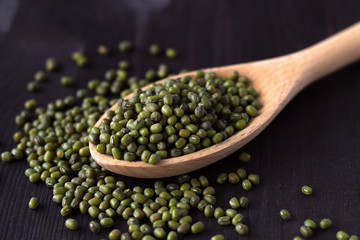  close-up mung beans in a wooden spoon. green mung beans in spoon on a black background. copy space. Healthy lifestyle. wooden spoon with dried mung beans on a wooden table.