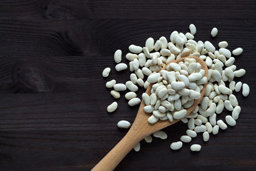 wooden spoon with dried white beans on a wooden table. Healthy lifestyle. white beans in spoon on a black background. copy space. top view.