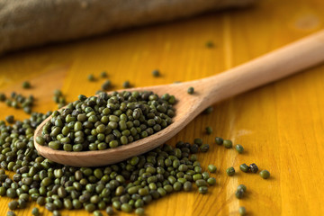 green mung beans in spoon with sackcloth on a yellow background. wooden spoon with dried mung bean and burlap on a wooden table. copy space. Healthy lifestyle.