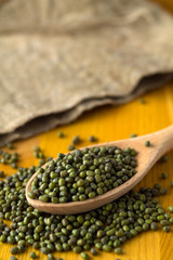 green mung beans in spoon with sackcloth on a yellow background. wooden spoon with dried mung bean and burlap on a wooden table. copy space. Healthy lifestyle. vertical