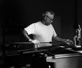 Middle Aged man measuring metal bar at workbench, black and white