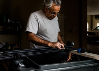 Older man using angle grinder in home workshop, sparks flying