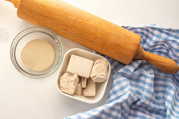 dried and fresh yeast on a white kitchen bacground with wooden rolling pin