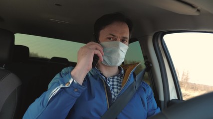Fototapeta na wymiar boy is driving and talking on android. Healthy young guy in protective sterile medical mask drives a car. Free man with mobile phone travels in mask in car. protection against viruses and bacteria.