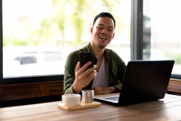 Fototapeta na wymiar Happy young Asian man video calling at the coffee shop