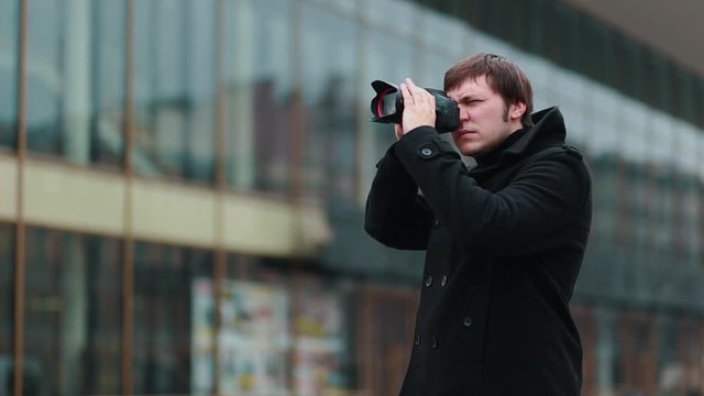 A photographer in a black coat stands on the street making a series of frames