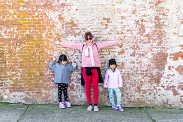 Mommy and her identical twins happy pose with old brick wall background.
