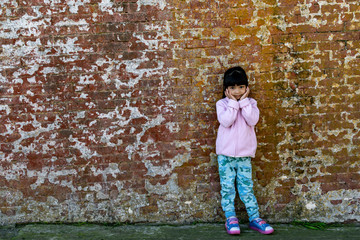 Fototapeta na wymiar Asian female child wearing pink jacket cute pose with old brick wall background