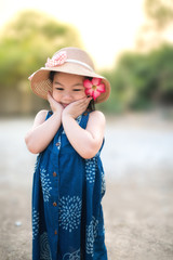 Cute Asian little girl is wearing a blue dress and wearing a brown hat in the park on a spring day.