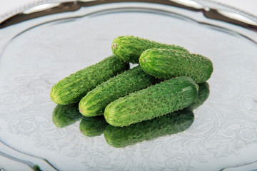 Fresh green pickling cucumbers on metal tray with folk ornament