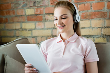 smiling woman in wireless headphones using digital tablet in living room