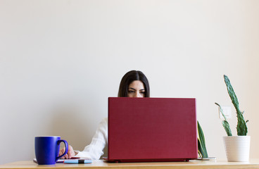 Front view of casual woman working from home during confinement season, due to Covid. Telecommuting. With a cup of coffee on the table.
