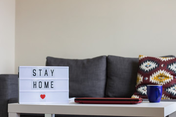 Home interior, where you can see, sofa in the background and focused, laptop, cup of coffee and panel where it puts in English, stay at home.