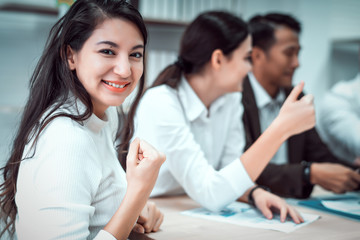 Young confident Asian business woman smiling and sitting in front of business team meeting or brainstorming at office. Teamwork meeting and partnership conference working concept.