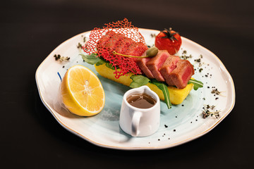 Slices of red meat with lemon and tomato on a white plate. Black outlined background.