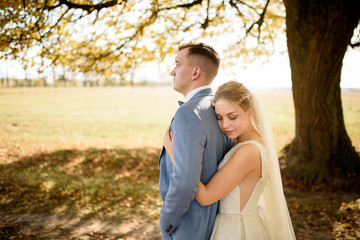 Young beautiful couple hugging in their wedding dresses in autumn park.