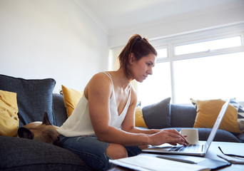 Female drinking coffee whilst working on sofa.