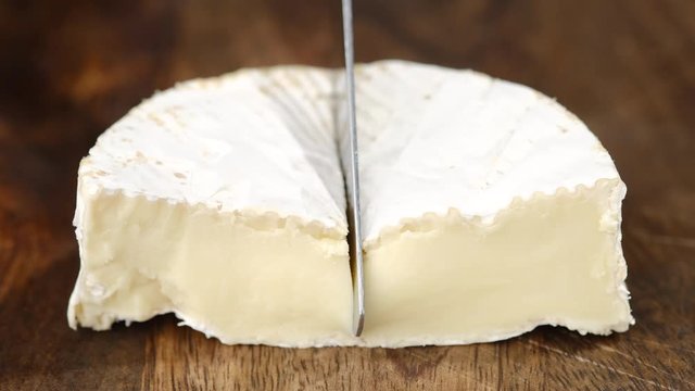 cutting soft cheese camembert or brie with knife closeup. creamy soft cheese inside. white mold cheeses with soft textures. wooden board