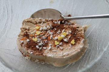Cream brulee ice cream with cinnamon and coconut shavings, with a spoon in a glass dish. Preparing a delicious dessert