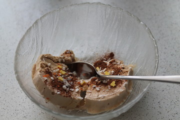 Cream brulee ice cream with cinnamon and coconut shavings, with a spoon in a glass dish. Preparing a delicious dessert