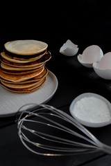
Pancakes and products for cooking, eggs, flour. Whisk for whipping on the table. Black background.