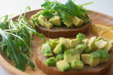 Healthy  breakfast toasted rye bread with avocado, arugula, lemon juice, salt and pepper on a wooden plate