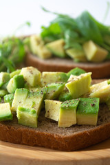 Healthy  breakfast toasted rye bread with avocado, arugula, lemon juice, salt and pepper on a wooden plate