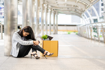 An unemployed woman sitting with her box of office properties. She was dismissed due to the economic downturn and the coronavirus outbreak. Layoff and coronavirus concept.