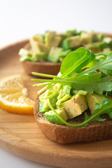 Healthy  breakfast toasted rye bread with avocado, arugula, lemon juice, salt and pepper on a wooden plate