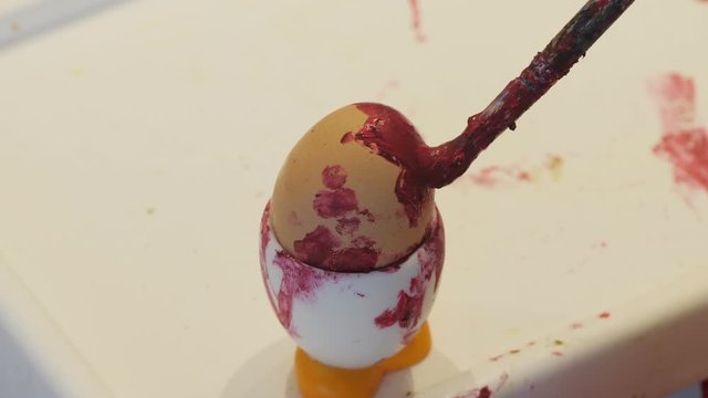 Little brush paints boiled egg with red paint.