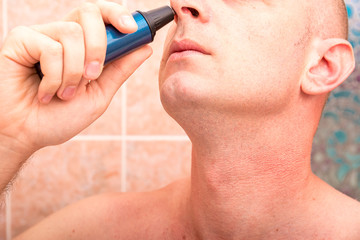 Close-up of a male nose with a trimmer near it, in bathroom. Removal of excess hair. The concept of hygiene, self-care.