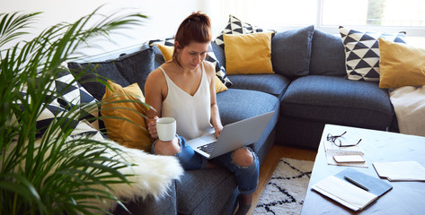 Young female working on tablet computer sat on sofa