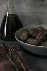 Plato de albondigas con botella de aceite de oliva la fondo y cubiertos dorados