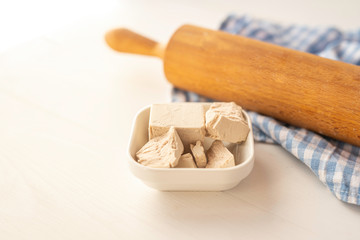 close up detail of fresh yeast cube  on a white background in a white porcelain dish with rollingpin  