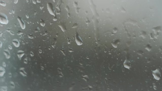 Close up of a window with rain drops falling down, Heavy rain on window. Rain splashing on a window, over a cloudy blue sky. ULTRA HD. 4K.