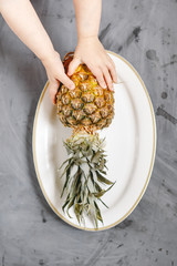White Plate with Ripe Whole Pineapple on Grey Concrete Background.