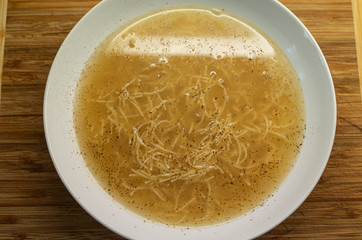 Cooked Veal soup with egg noodles in a white bowl set on wood board in the kithen