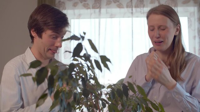 Cold sneezing young couple in bright interior of the room decorated with houseplants