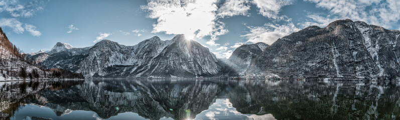 Panoramic view of snowy Hallstatt village houses at foot of mountain by lake with reflection in winter in Austria