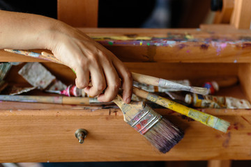 Paint artist's hand with brushes for painting on easel. Dirty easel