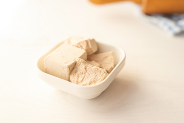 close up detail of fresh yeast cube  on a white background in a white porcelain dish 