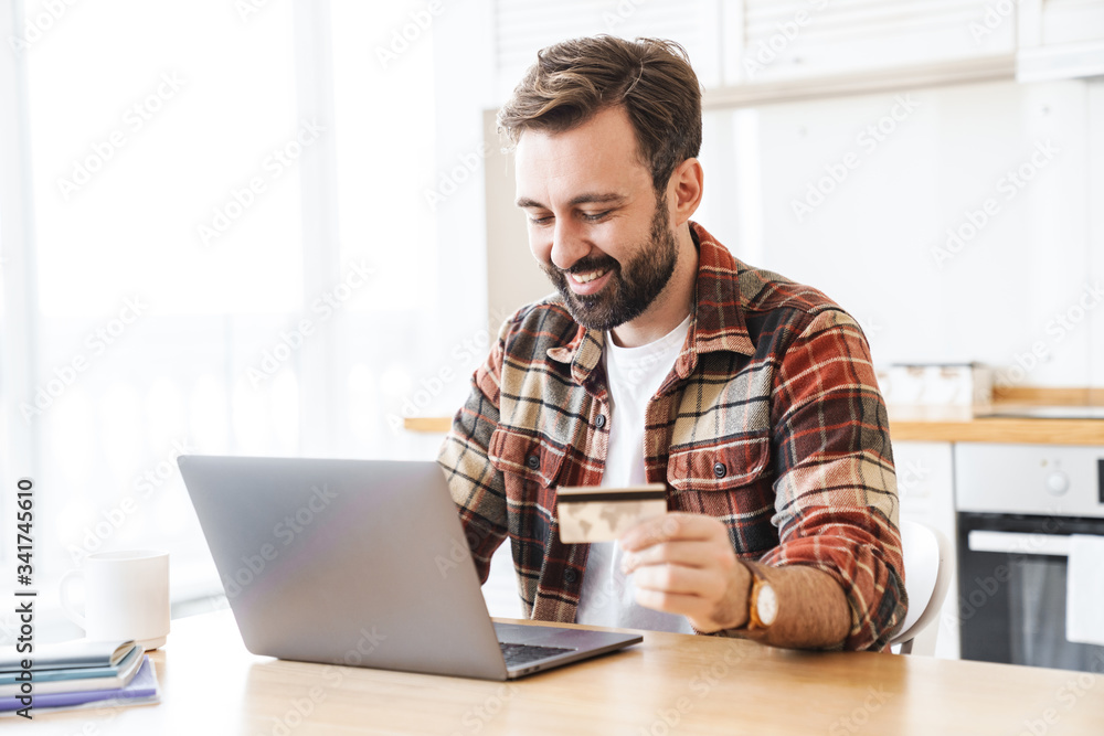 Poster Portrait of cheerful man working with laptop and holding credit card