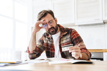 Portrait of young serious man holding credit card while working at home