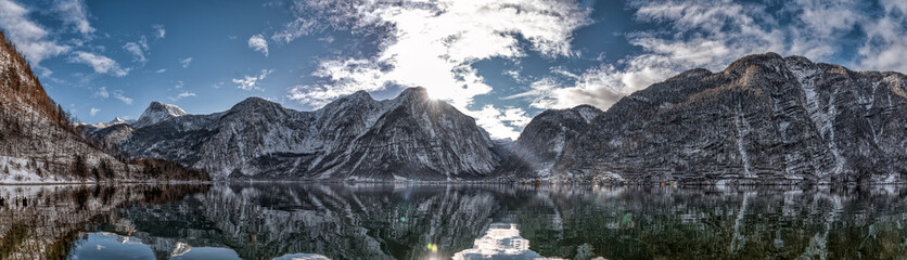 Panoramic view of snowy Hallstatt village houses at foot of mountain by lake with reflection in winter in Austria