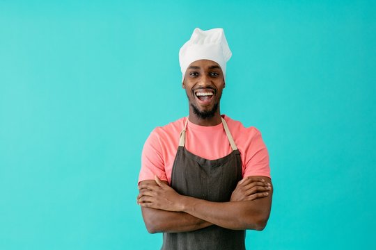 Portrait of an excited young male chef with arms crossed and mouth open, against blue studio background